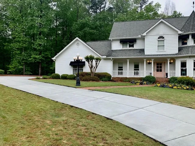 Long two car wide concrete driveway wrapping around the front a home