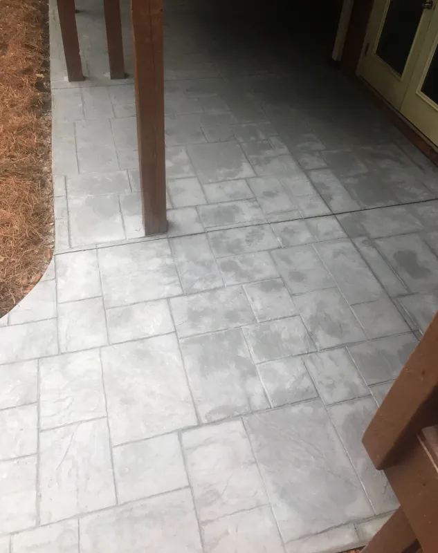 A grey stamped concrete patio shadowed by a deck overhead.